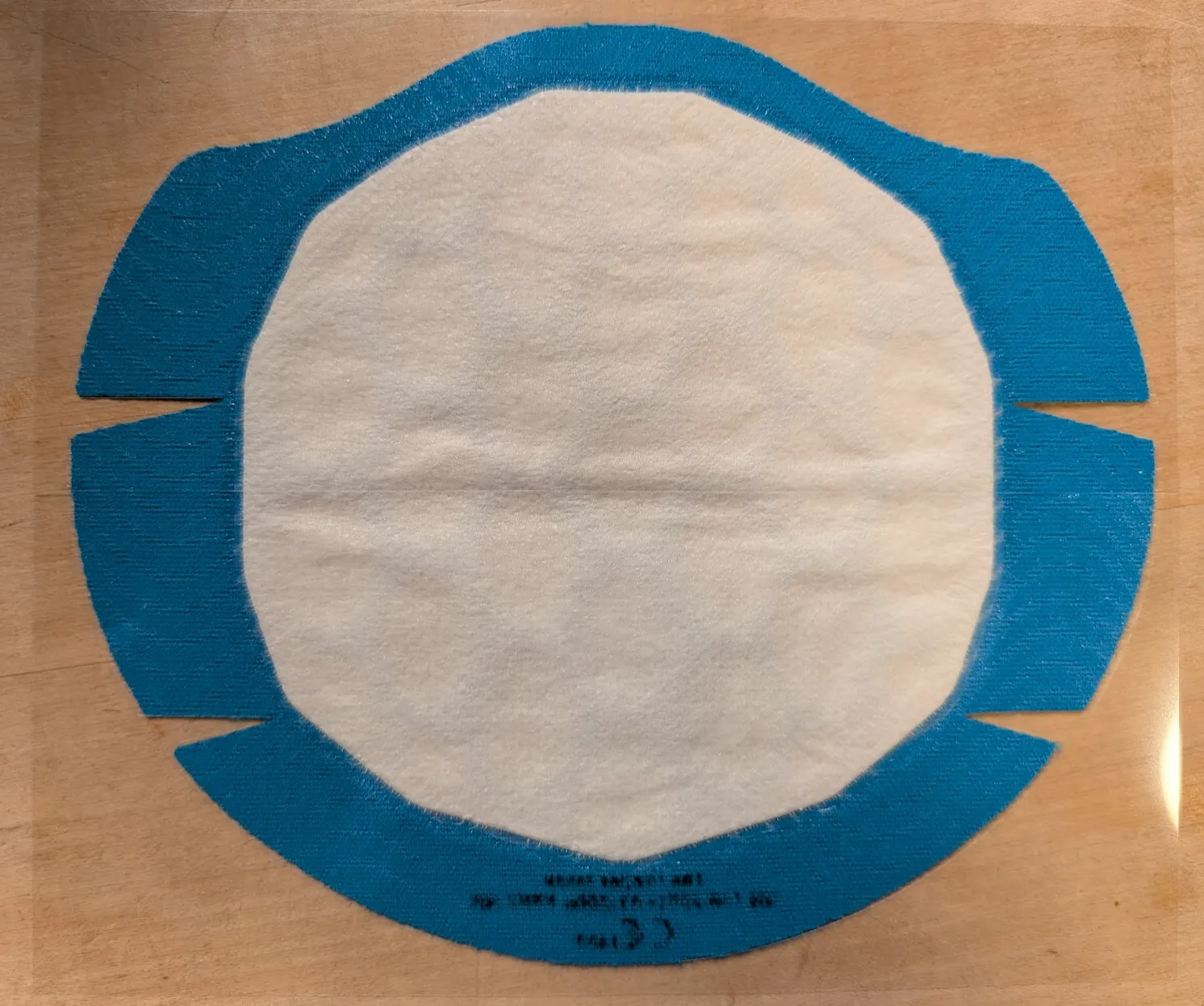 The Proper Mask flach ausgelegt: blauer Klebestoff mit aufgeklebtem weißem Filtermaterial